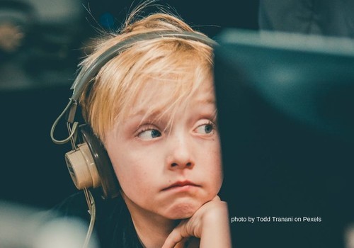 School child in headphones next to computer monitor